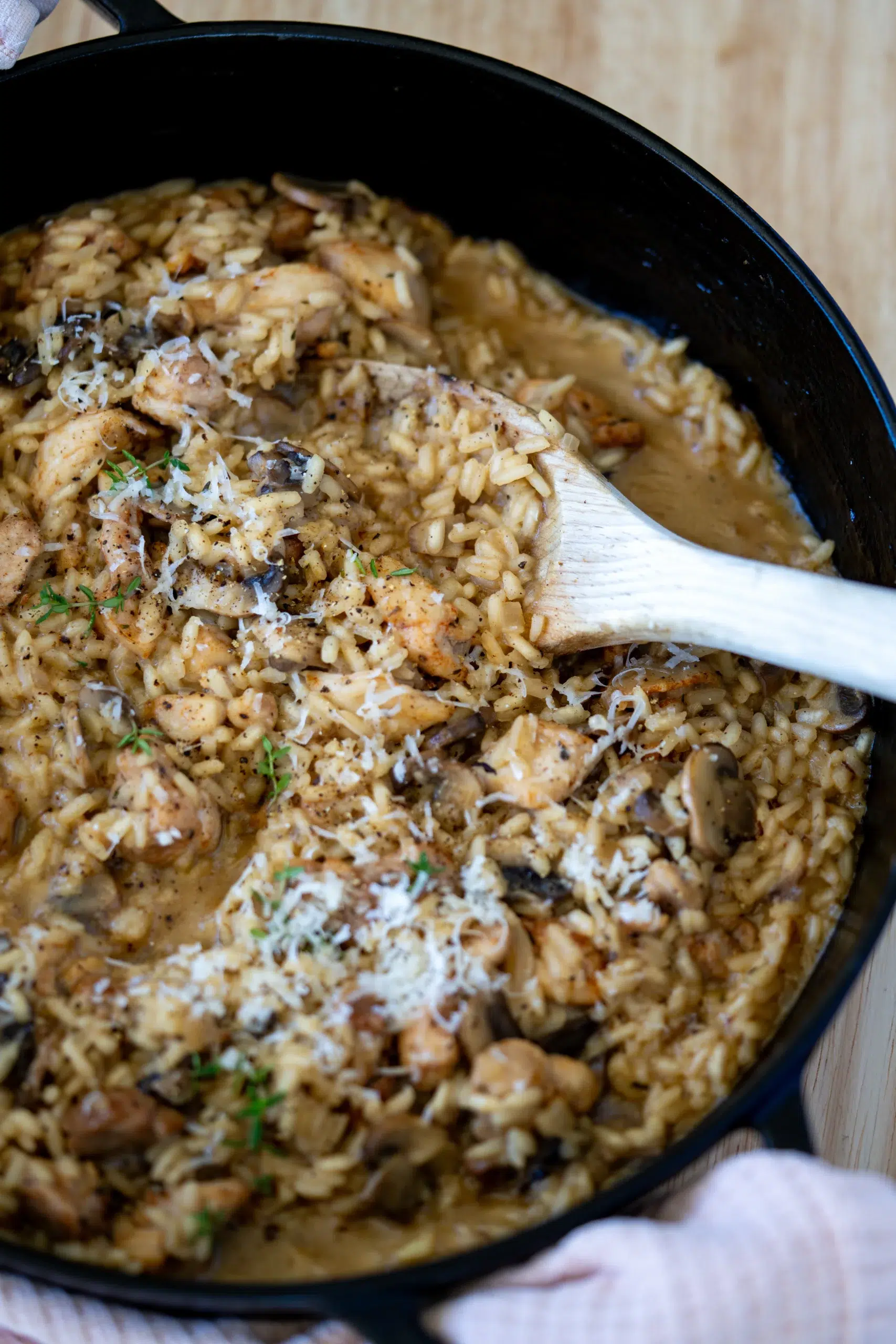 Creamy chicken and mushroom risotto in a black cast iron pan, stirred with a wooden spoon and topped with Parmesan and fresh herbs.