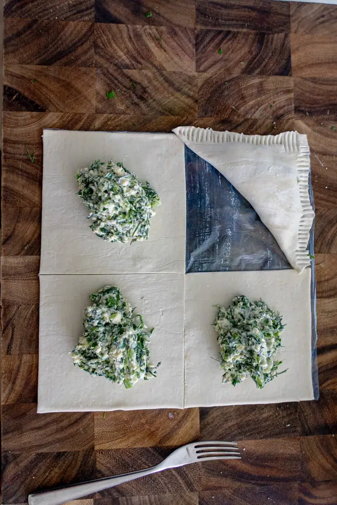 Puff pastry sheet cut into four squares with spinach and feta filling placed in one square