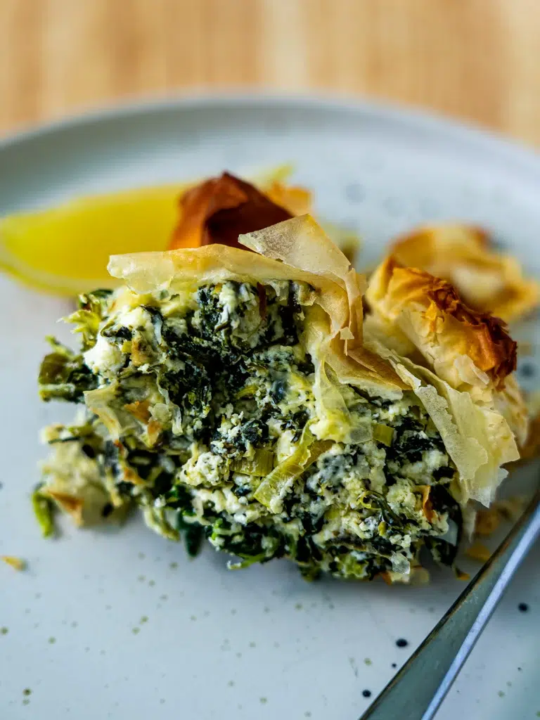 Served spanakopita on a plate, highlighting its crispy pastry and spinach filling, with a fork."