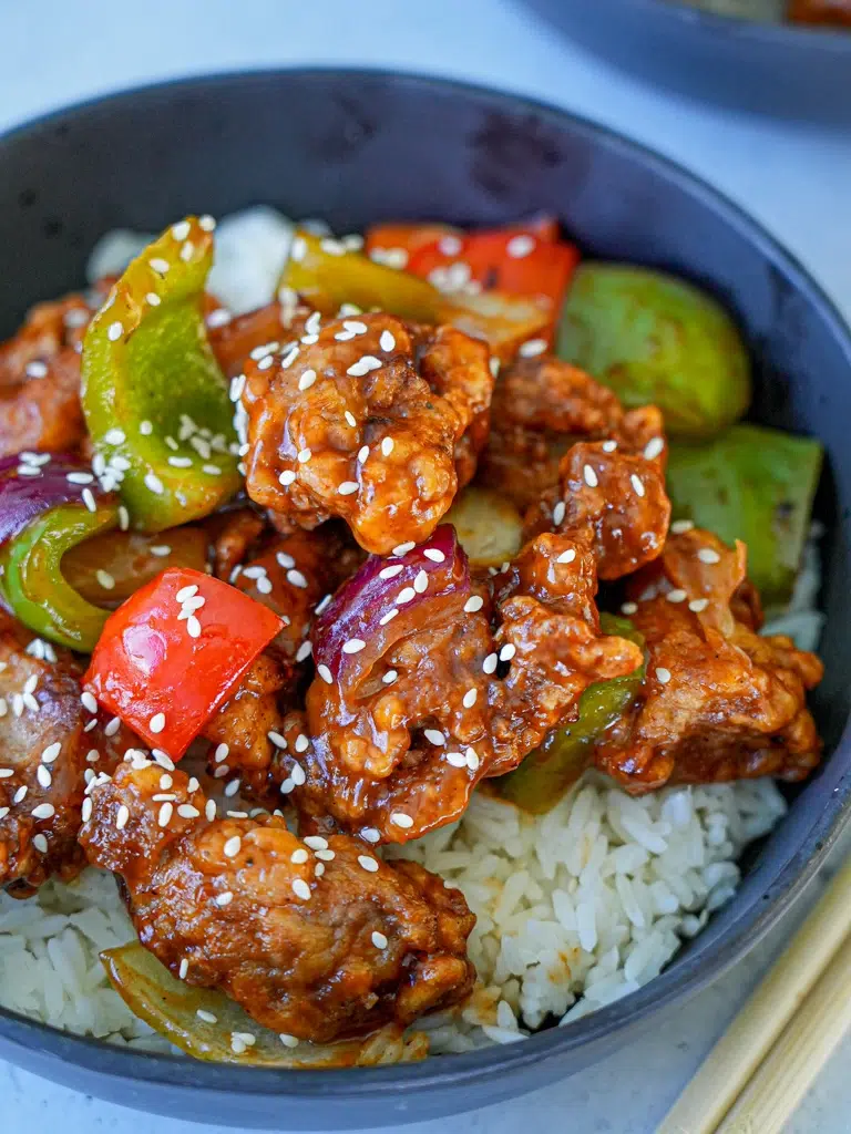 A vibrant bowl of sweet and sour pork featuring chunks of meat, diced bell peppers in a rich sauce.