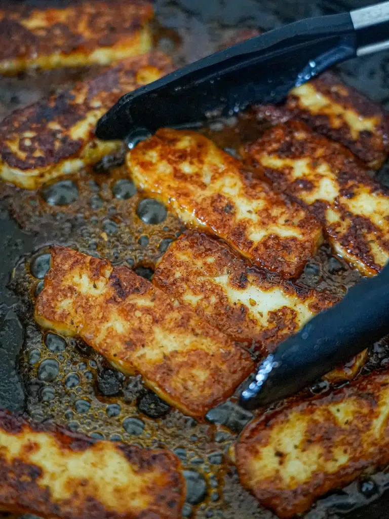 Golden slices of halloumi frying in a pan, sizzling in hot honey sauce.