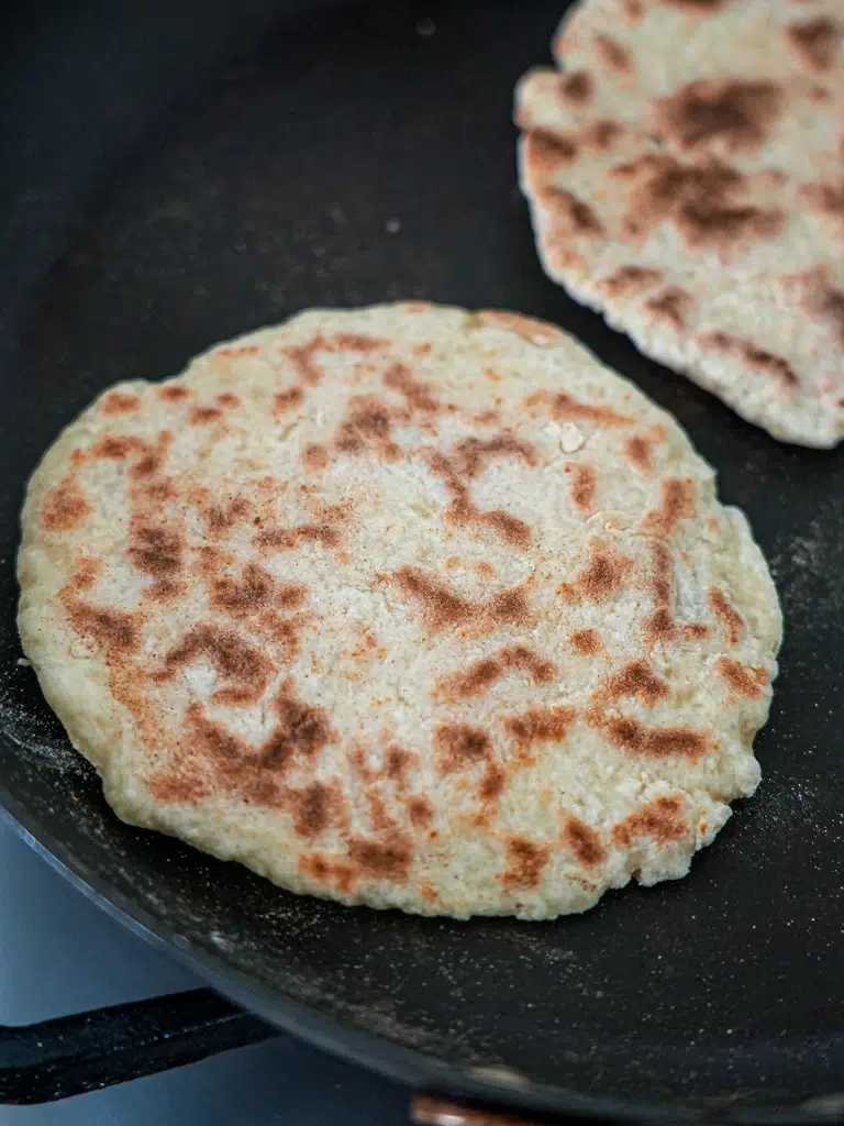 Flatbreads cooking in a pan until golden and puffed.