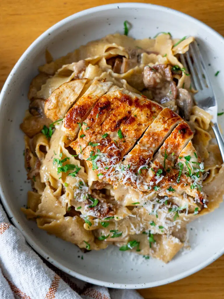 Top view of plated Chicken Boscaiola Pasta with creamy sauce, bacon, and mushrooms.