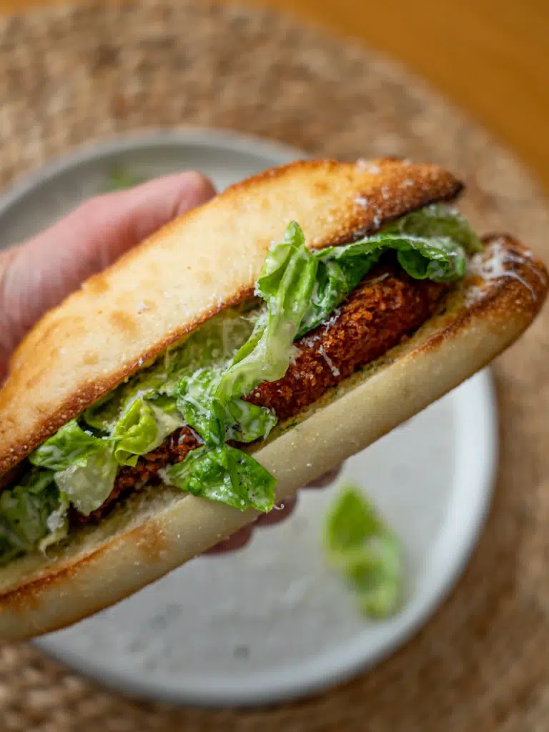Close-up of a hand holding a Crispy Chicken Caesar Sandwich with crispy chicken and Caesar dressing.