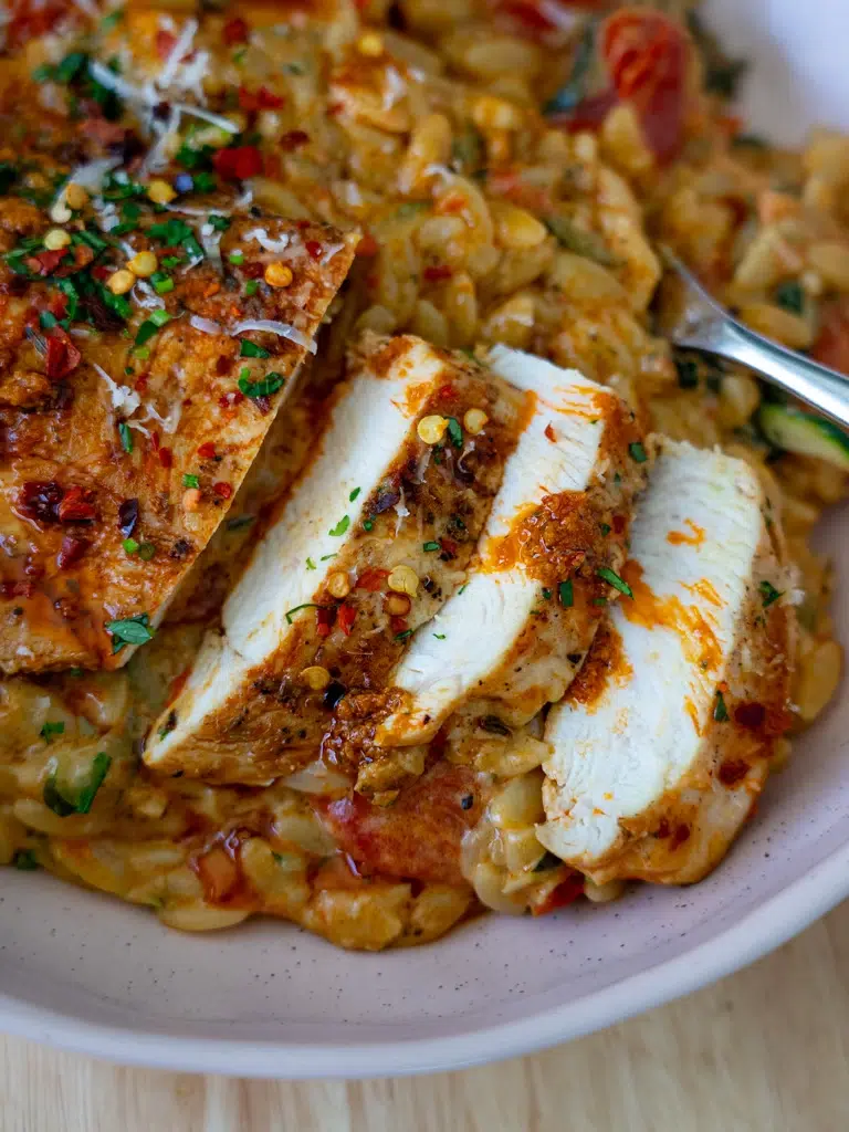 Sliced chicken served with creamy red pesto risoni on a serving plate.