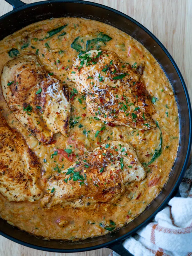 Top view of chicken with creamy red pesto risoni served in a pan.