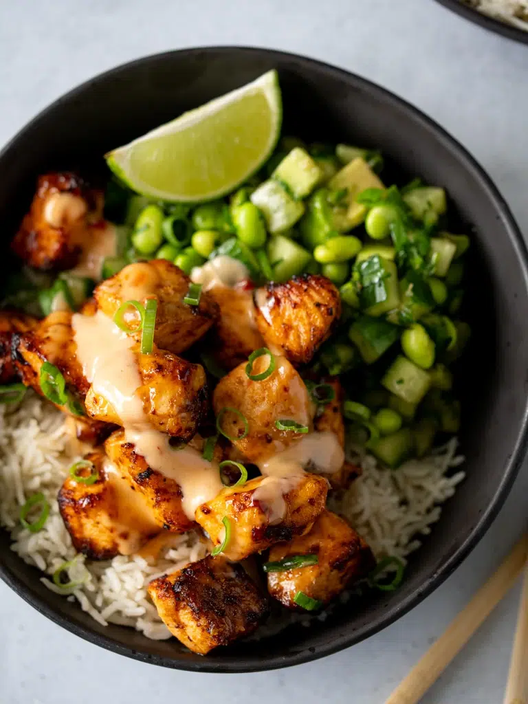 Close-up of crispy Bang Bang salmon coated in creamy sauce, highlighting the texture and glaze, served in a black bowl.