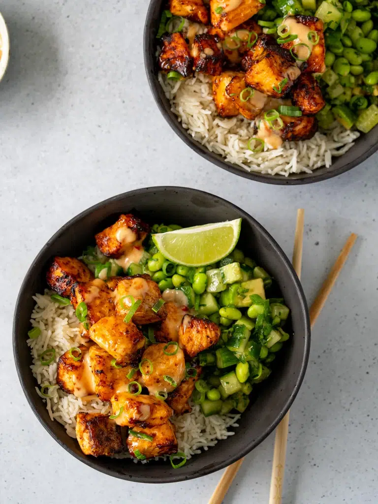 Overhead shot of two black bowls filled with Bang Bang salmon, drizzled with creamy sauce.