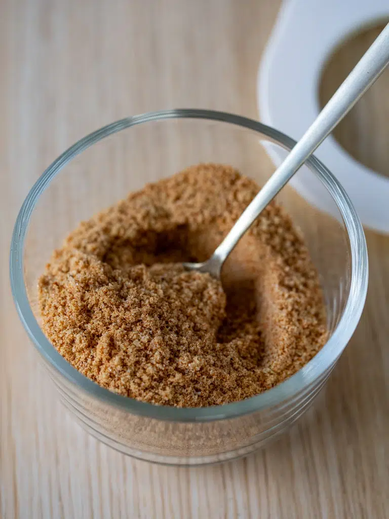 Glass jar of homemade chicken salt with a spoon, on a wooden surface.