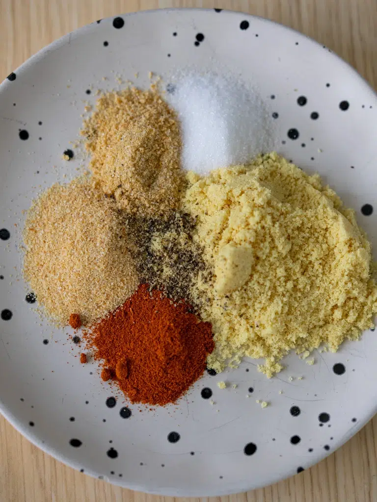 Individual spices for homemade chicken salt seasoning arranged on a white plate with black speckles.