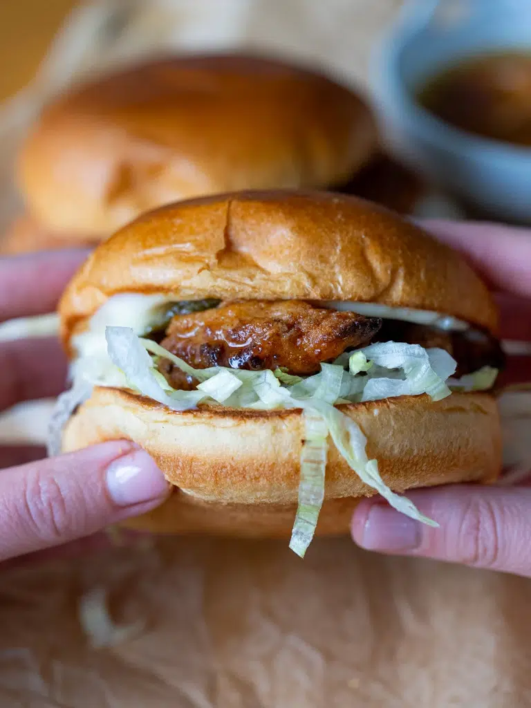 Hands holding a hot honey crunch chicken burger with crispy chicken, shredded lettuce, and soft brioche bun.
