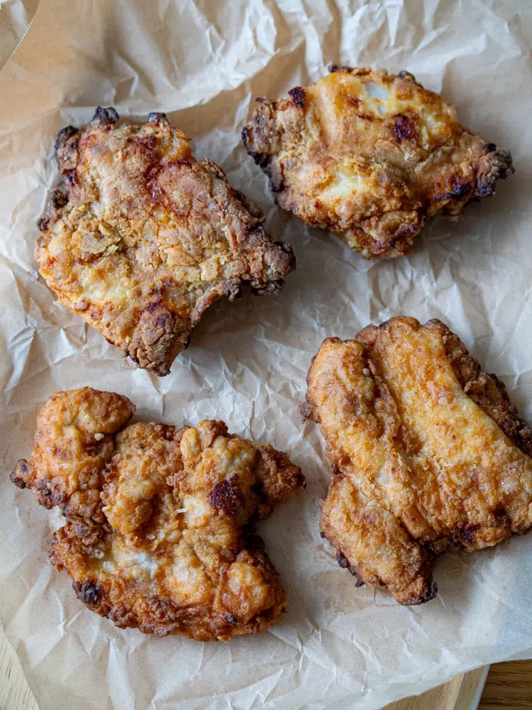 Four pieces of freshly fried crispy chicken thigh fillets resting on brown parchment paper.