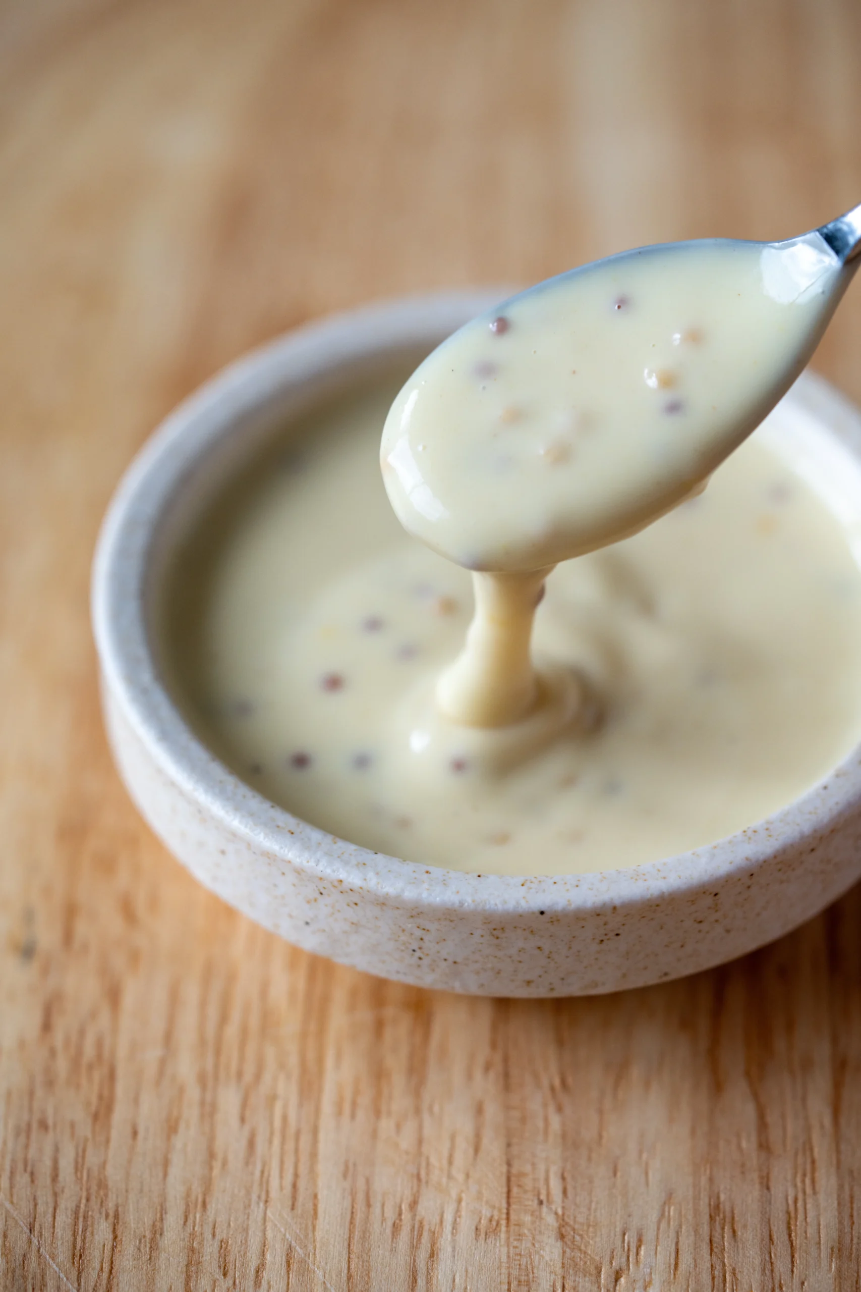 Creamy honey mustard dipping sauce in a small bowl, with a spoon lifting the sauce to show its smooth texture and mustard seeds.