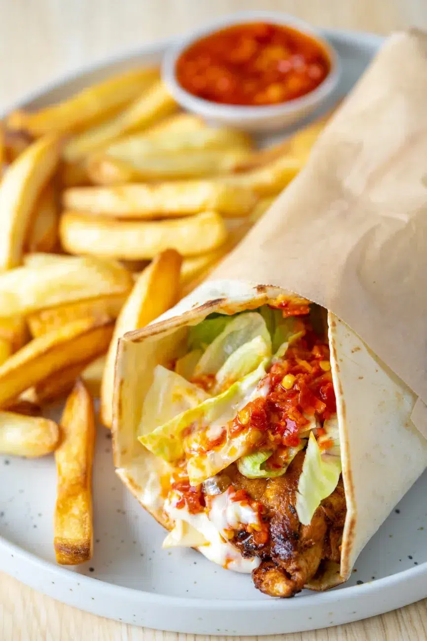 lose-up of Portuguese-style chili chicken wrap with lettuce, sauce, and fries on a plate