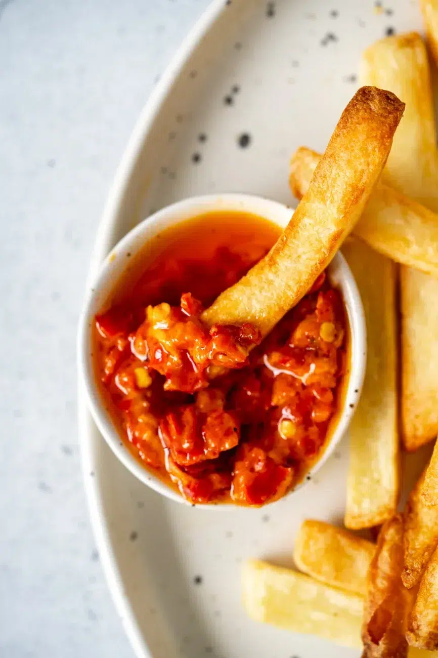 Close-up of golden fries dipped in Portuguese-style chili sauce with red chili pieces