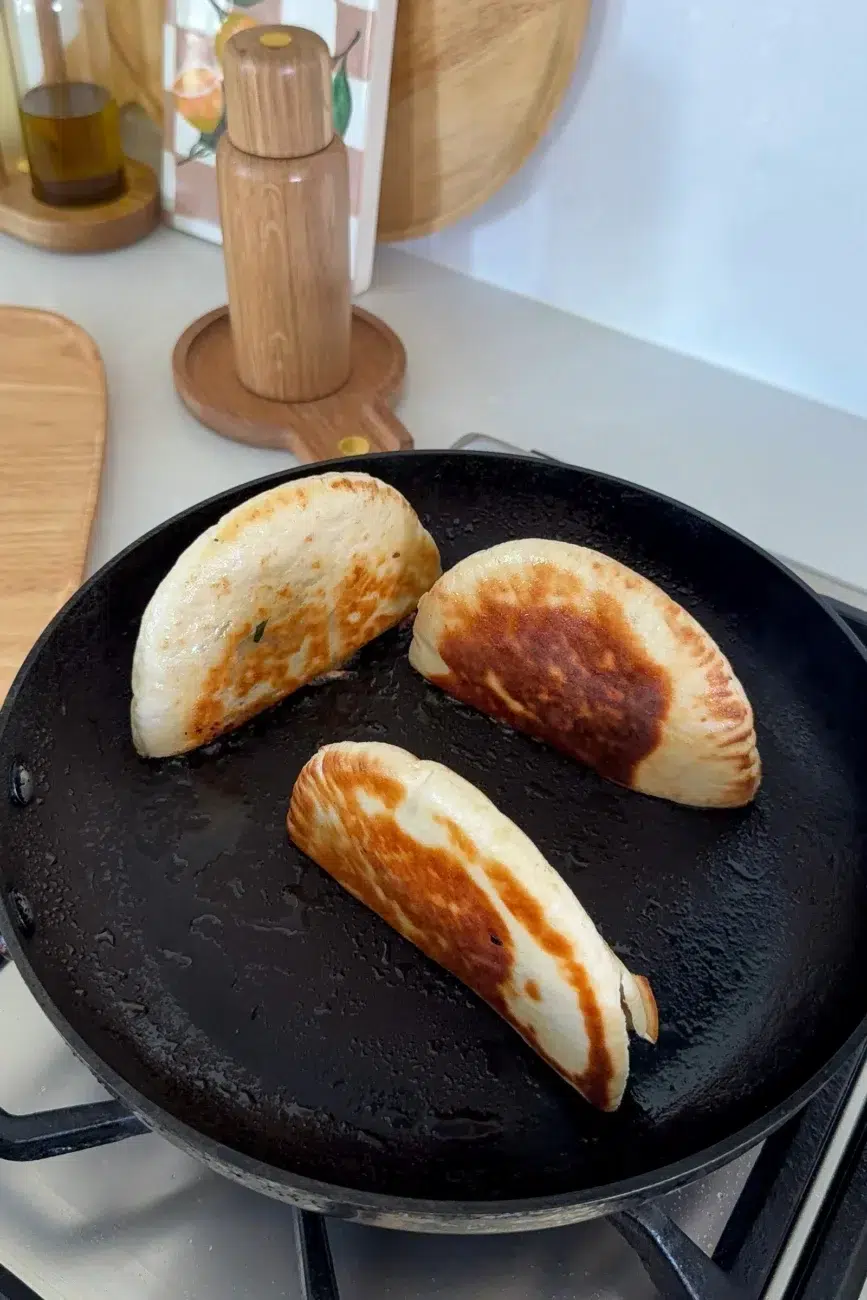 stuffed pita arayes being cooked in a pan edge side down